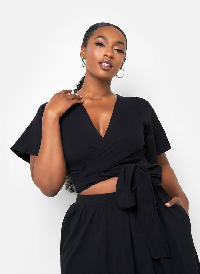 Woman in a stylish wrapped black top and skirt poses confidently