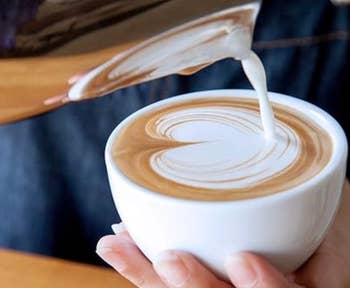 Model pouring milk into a coffee cup creating a heart-shaped latte art