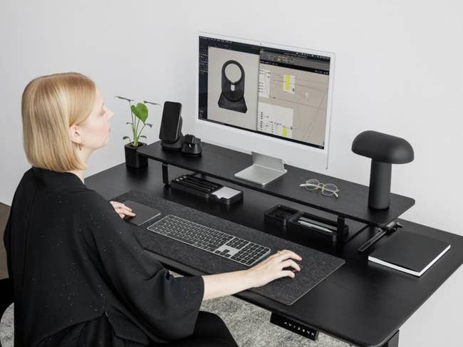 model working at a desk with a monitor on the black wood stand