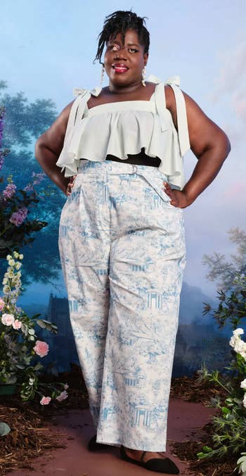 model posing in a ruffled top and printed trousers against a floral backdrop