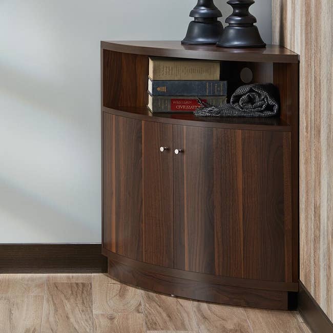 a dark wood corner cabinet with two doors and a small shelf on top