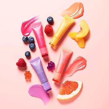 Assorted skincare products with fruit slices and gummy bears arranged on a pink background