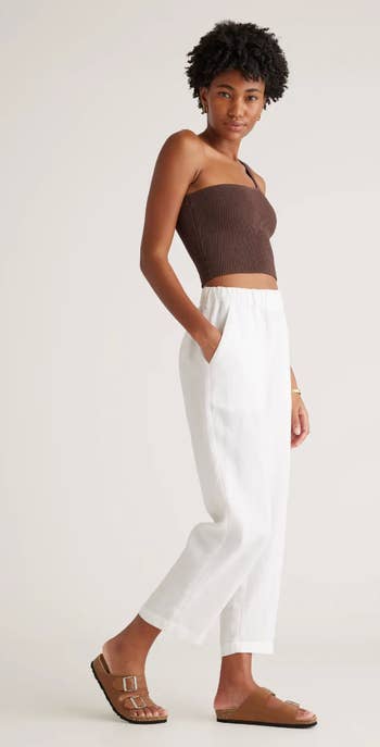 Model in a strapless ribbed top with white linen trousers and brown slide sandals