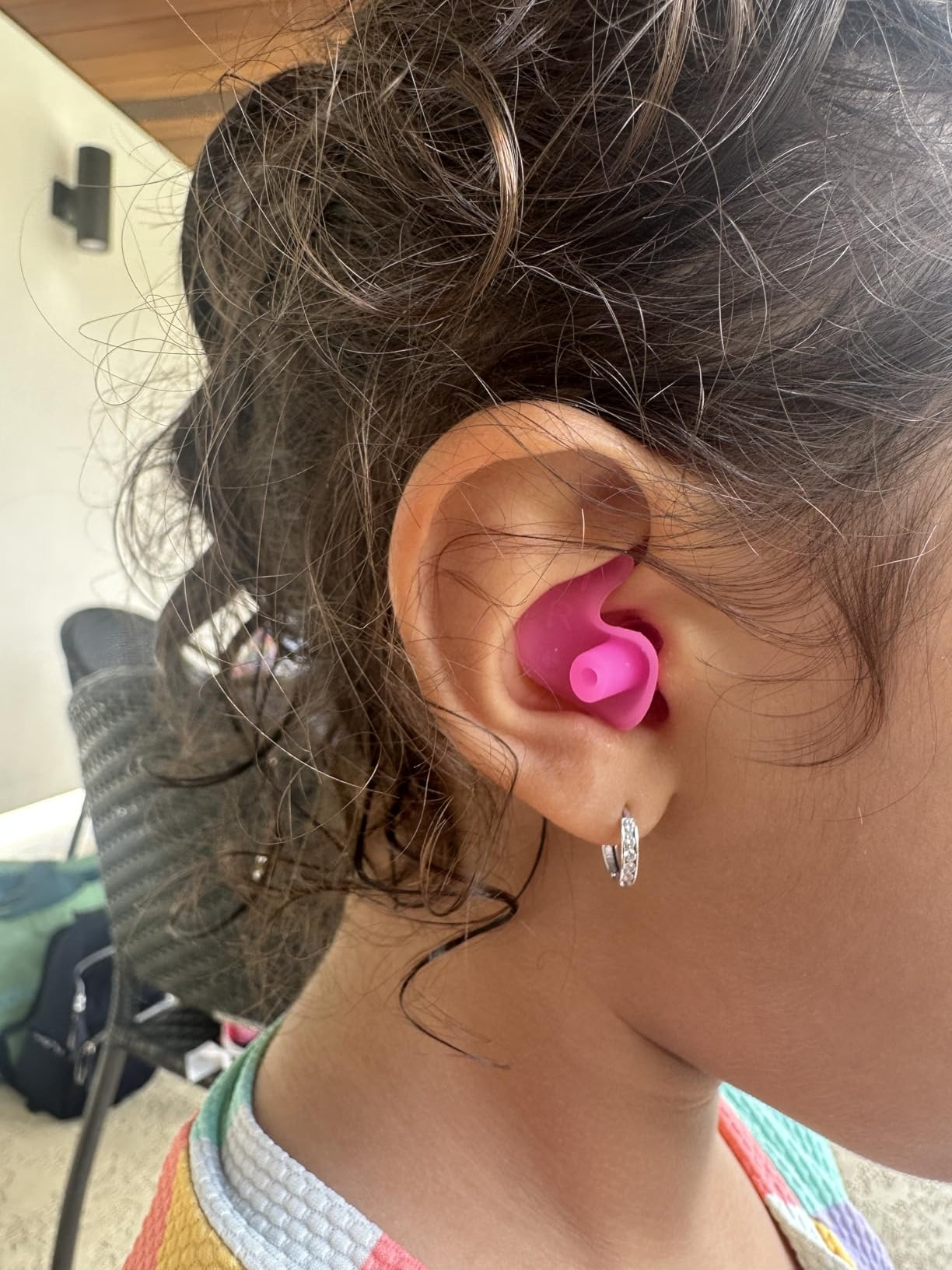 Child wearing pinkish  silicone earplugs, focusing connected  close    receptor  with curls