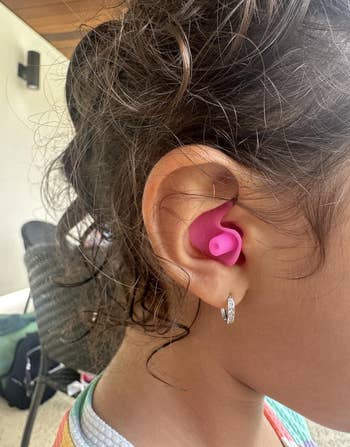 Child wearing pinkish silicone earplugs, focusing connected close receptor with curls