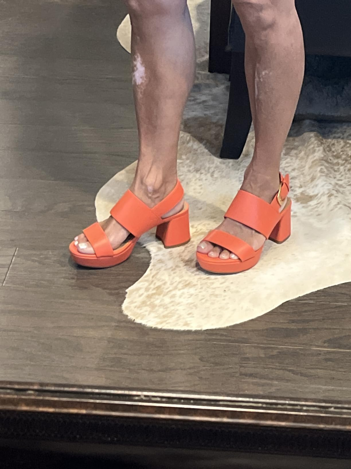 Person wearing orangish  level    sandals with heavy   straps, lasting  connected  a wood   level  with a patterned rug