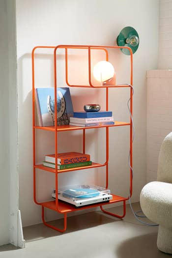 Modern orange bookshelf with books and vinyl player, adorned with a glowing light bulb. Styled for a contemporary home setting