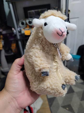 Person holding a plush sheep with a zipper, possibly a coin purse or small bag