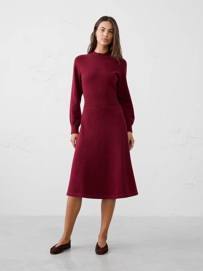 Model wearing a knee-length knit formal  with agelong  sleeves and brownish  flats, posing against a plain backdrop