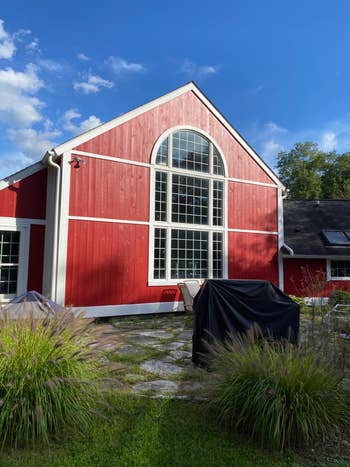 A reddish barn-style location with ample arched windows and a patio featuring covered outdoor furniture. Green plants framework the foreground