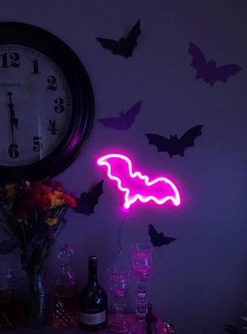 the neon pink bat sign on a reviewer's wall next to paper black bats