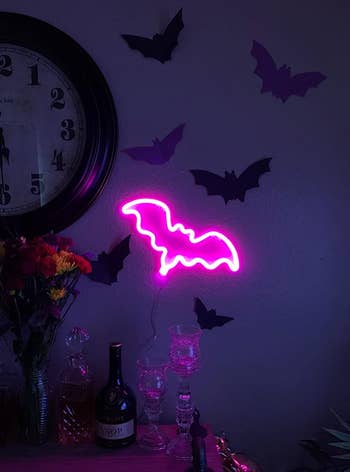 the neon pink bat sign on a reviewer's wall next to paper black bats