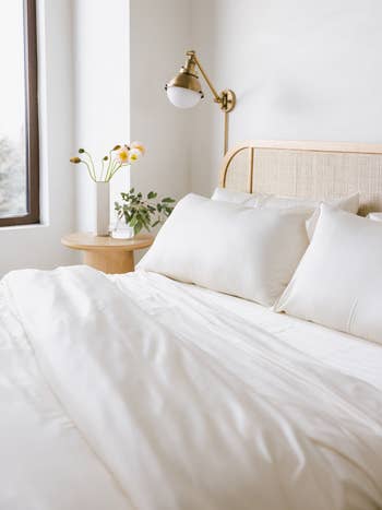 Cozy chamber with a neatly made bed, achromatic pillows, a bedside table, flowers successful a vase, and a partition lamp by the window