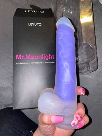 Reviewer holding transparent and purple realistic dildo