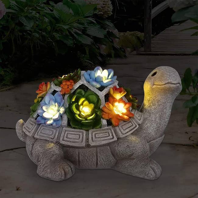 A gray ceramic turtle with lit up flowers on its shell 