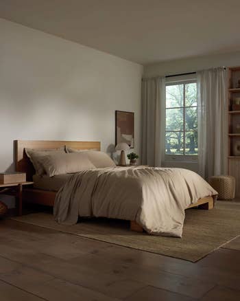 Minimalist chamber  with woody  bed, neutral bedding, broadside  table, ample  window, and shelves. Cozy rug and earthy  airy  make  a serene atmosphere