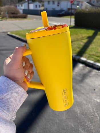 Person holds a ample insulated yellowish mug labeled