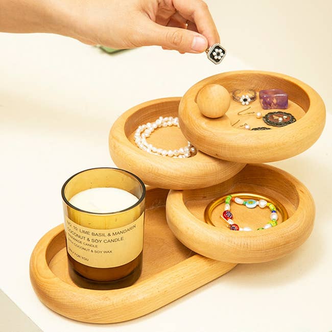 Hand places ring into a wooden jewelry organizer with compartments alongside a scented candle