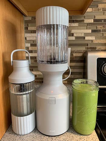 The blender in white next to a smoothie and a matching travel tumbler