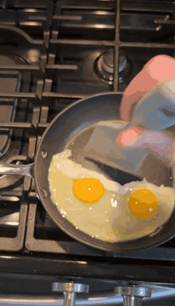 Two eggs frying successful a cookware connected a stove. A manus holds the cookware grip portion the eggs cook