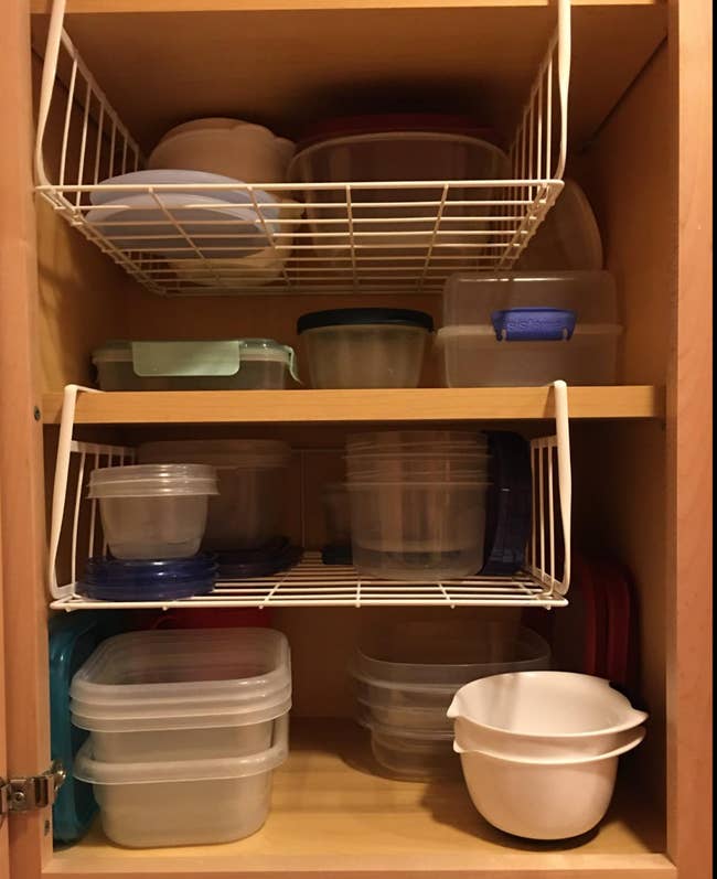 Two white wired shelves installed under cabinets and holding tupperware