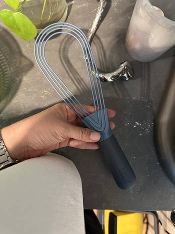 A manus  holding a blue, level  room  whisk with a achromatic  handle, designed for casual  storage, connected  a room  counter