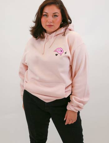 a  model wearing a light pink hoodie with a lip print on the upper left side 