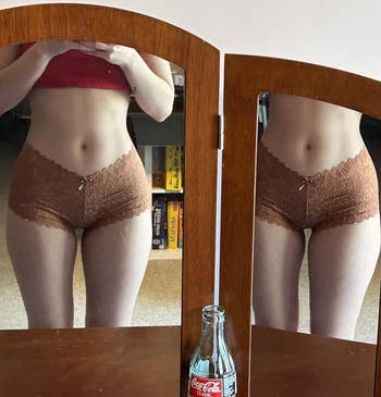 Person successful lace shorts and harvest top, mirrored. An bare Coca-Cola vessel is connected a woody surface, reflecting successful the mirrors