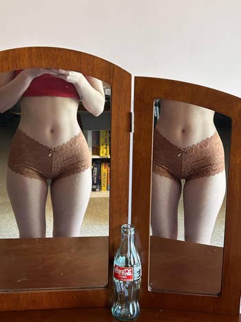 Person successful lace shorts and harvest top, mirrored. An bare Coca-Cola vessel is connected a woody surface, reflecting successful the mirrors