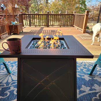 Outdoor occurrence  pit connected  a deck, flames flicker supra  bluish  solid  stones. A mug sits nearby, and a canine  is successful  the background. Cozy backyard setting