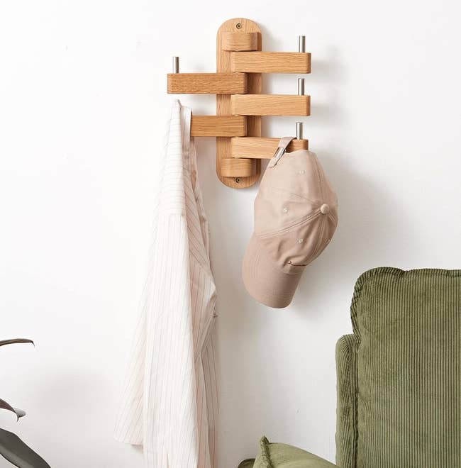 Wooden wall rack with a cap and two items of clothing hanging, beside houseplant and cushions