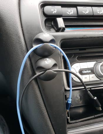 a reviewer photo of the cable clips mounted on a car dashboard each holding a cord 