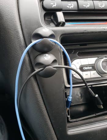 a reviewer photo of the cable clips mounted on a car dashboard each holding a cord 