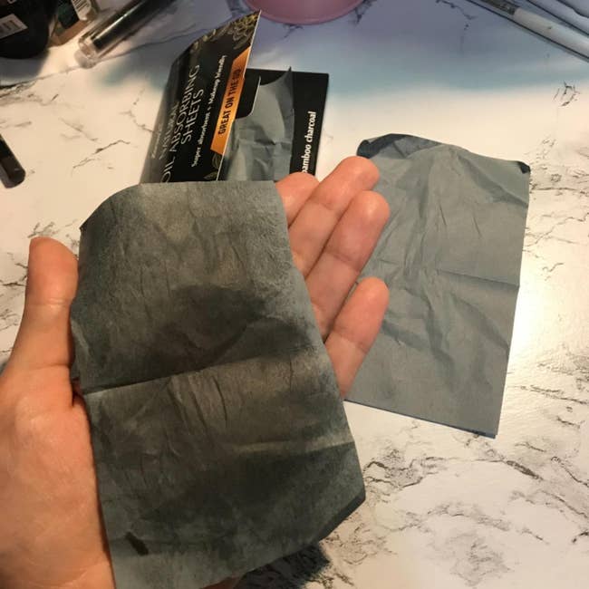 A reviewer holding a used blotting paper that absorbed the oil from their face