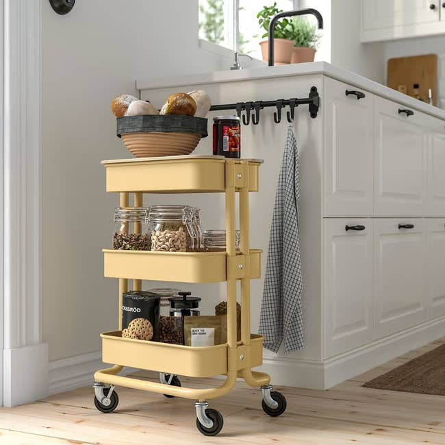 Kitchen with a wheeled cart holding jars and a hanging cloth, placed adjacent  to a achromatic  land  with potted plants