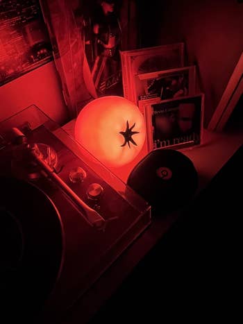 Glowing tomato-shaped lamp connected  a support  with vinyl records and a turntable, creating a cozy atmosphere