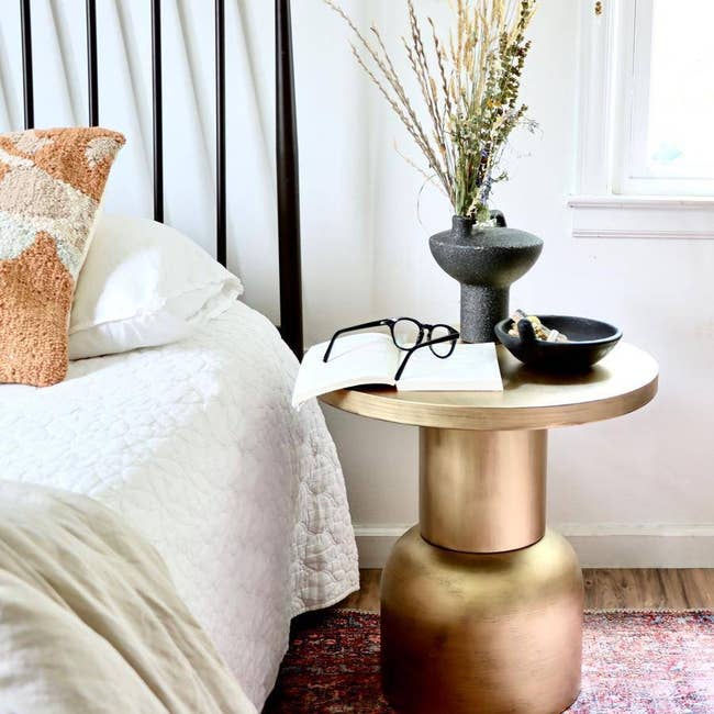 the antique brass finish accent table next to a bed