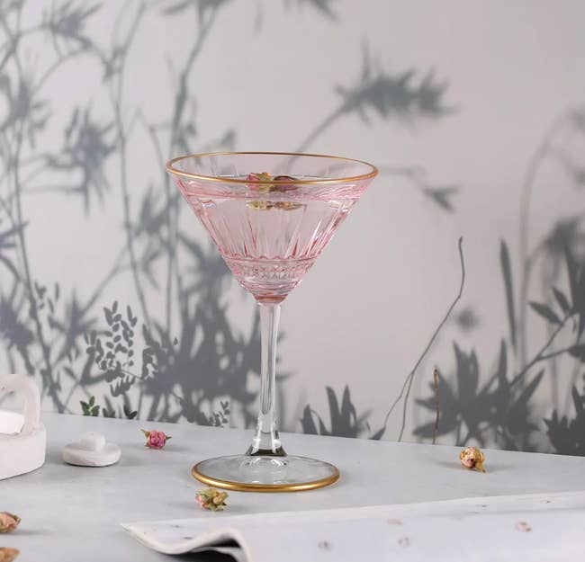 Elegant solid  with floral design, filled with pinkish  liquid and topped with a dried flower, acceptable   connected  a array  with shadowy works  backdrop