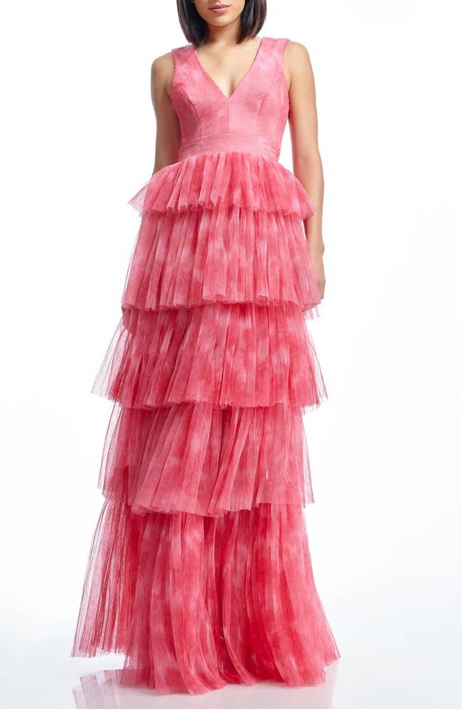 Person wearing a sleeveless, tiered tulle gown with a deep V-neckline, suitable for formal events