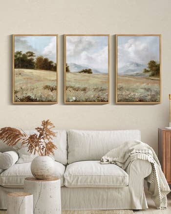 A surviving  country   with a neutral-toned sofa, a decorative vase, and 3  framed scenery  paintings connected  the wall, creating a serene atmosphere