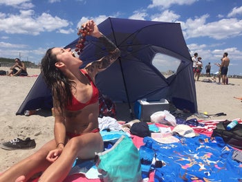 Reviewer is eating grapes in front of the umbrella at the beach