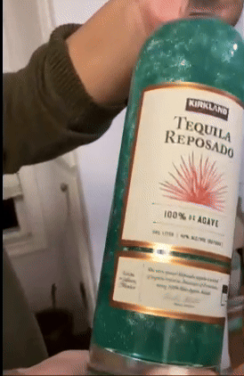 Person holding a shimmering green bottle of Kirkland Tequila Reposado