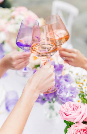 Four individuals toasting with rose wine in stem glasses over a floral adorned table