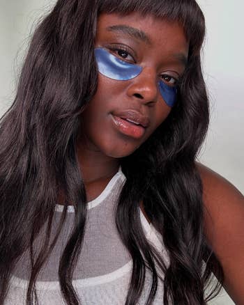 Person with agelong  hairsbreadth  wearing bluish  under-eye patches and a mesh top, posing for a skincare oregon  quality   merchandise  feature