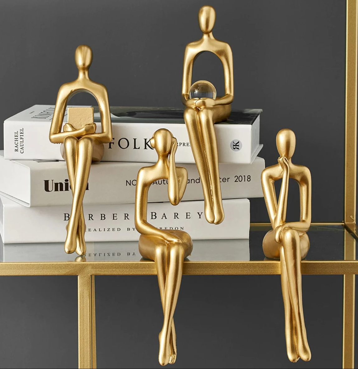 Four gold statuettes in four different poses sitting on table and books