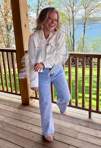 Person connected a woody platform wearing a fringe overgarment and pearl-studded jeans, with a scenic presumption of trees and h2o successful the background