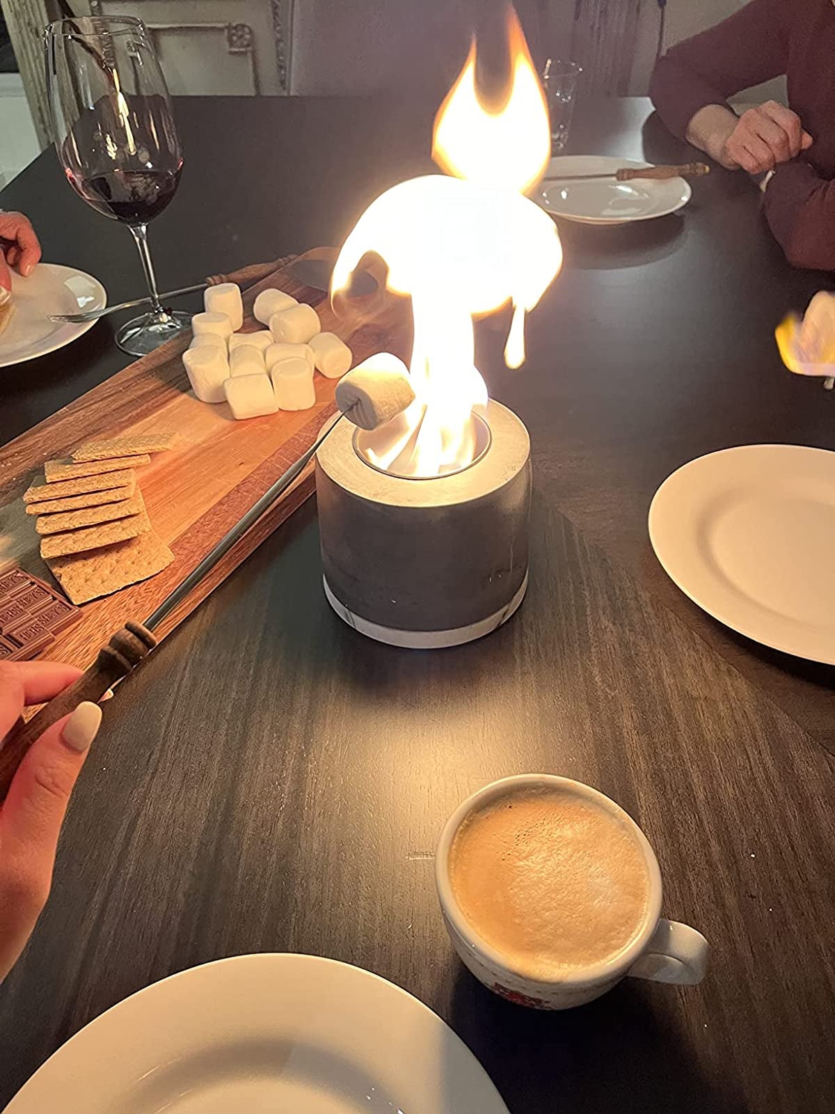 reviewer roasting a marshmallow over the lit tabletop fire pit