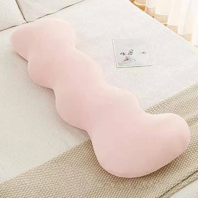 Curved body pillow on a bed next to an open book, suggesting comfort and relaxation