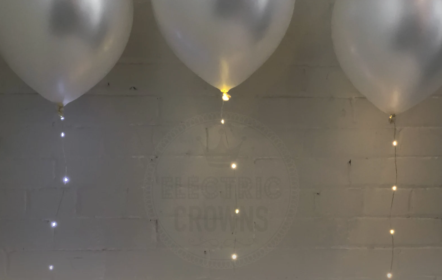 Three white balloons with with string light balloon strings in front of a white brick wall