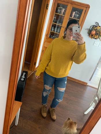 reviewer wearing same style sweater in a yellow color with distressed jeans and booties
